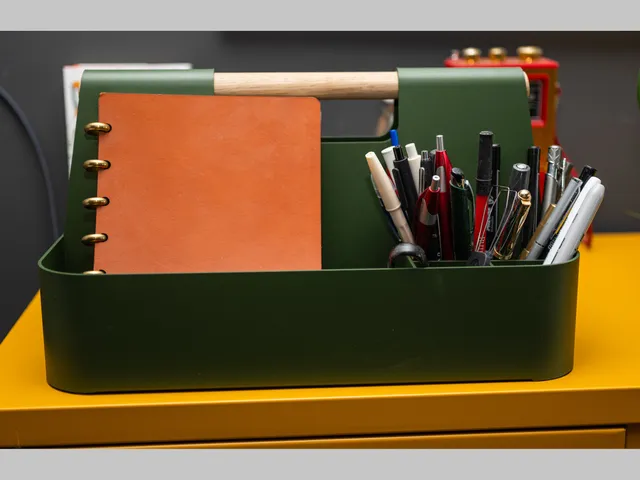 Branch Most Modest Desk Caddy in dark green, a rectangular container with components and a wooden handle, sitting on a yellow metal locker