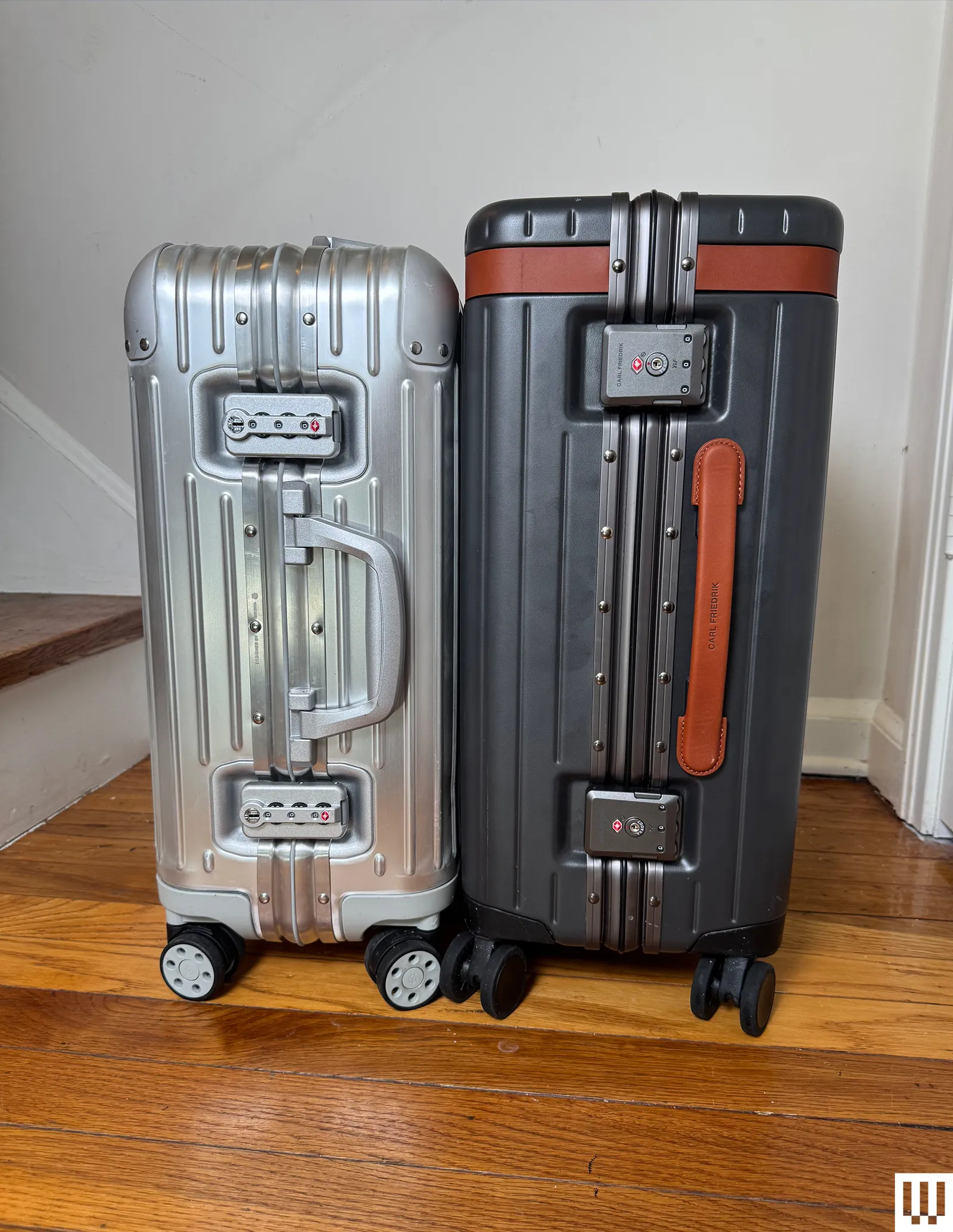 Side view of a silver Rimowa rolling luggage beside a black Carl Friedrik The Carryon rolling luggage