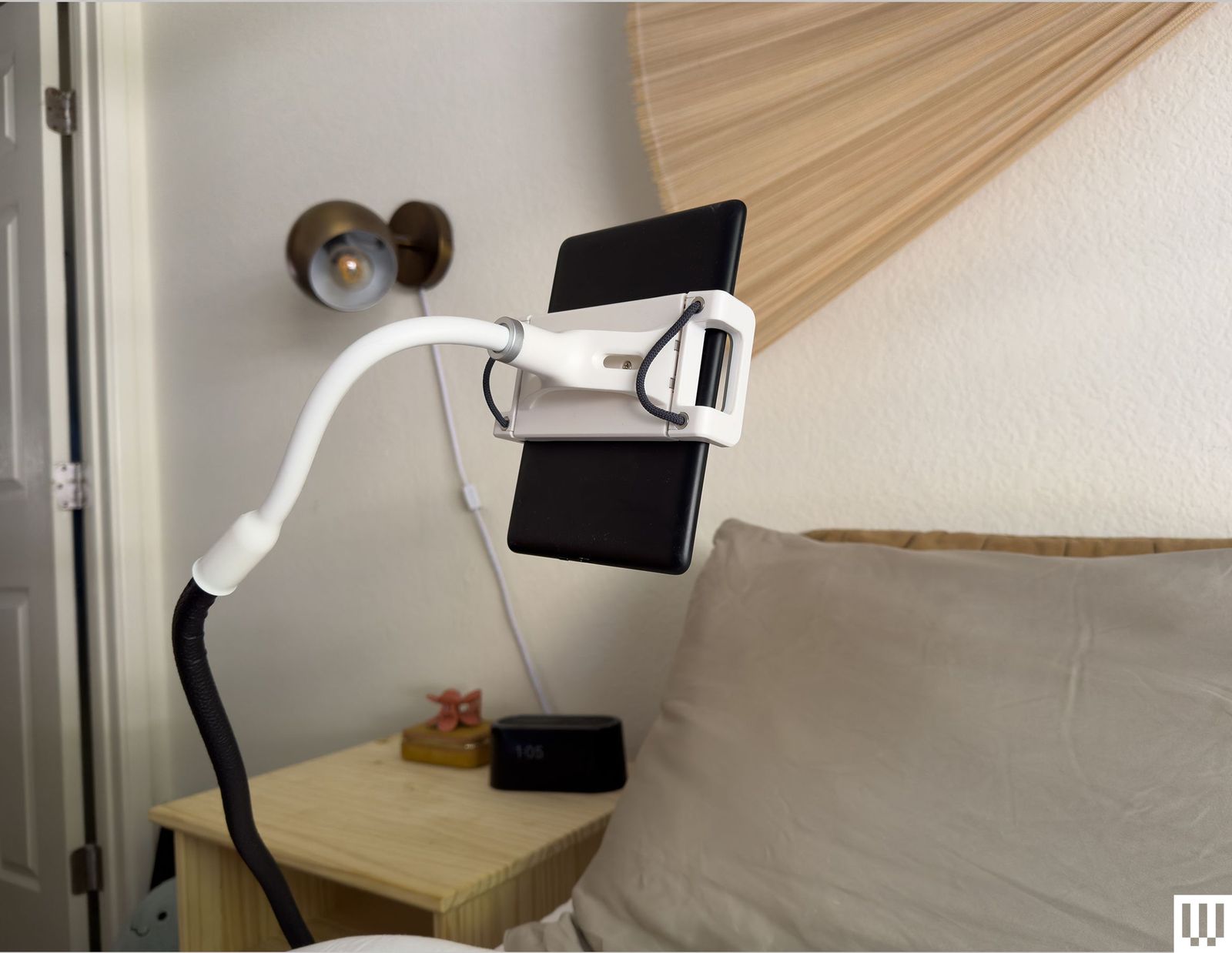 Black and white flexible stand holding a black tablet over a bed
