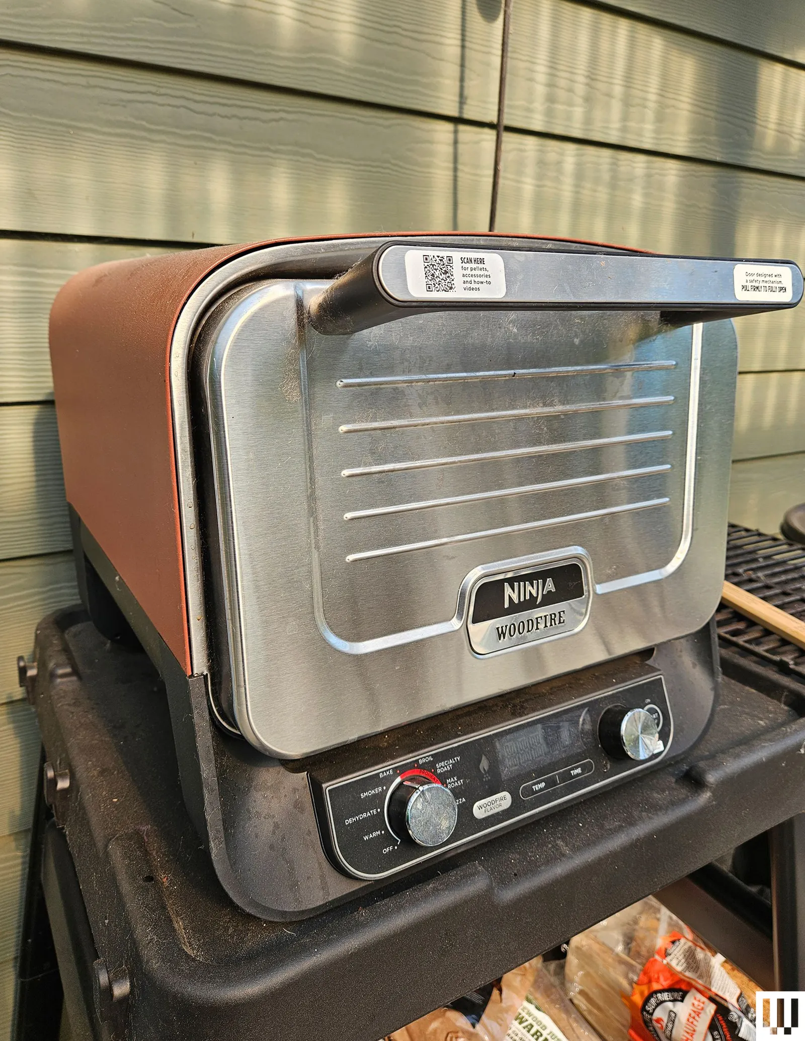 Small pizza oven sitting on a black shelf outdoors beside a house